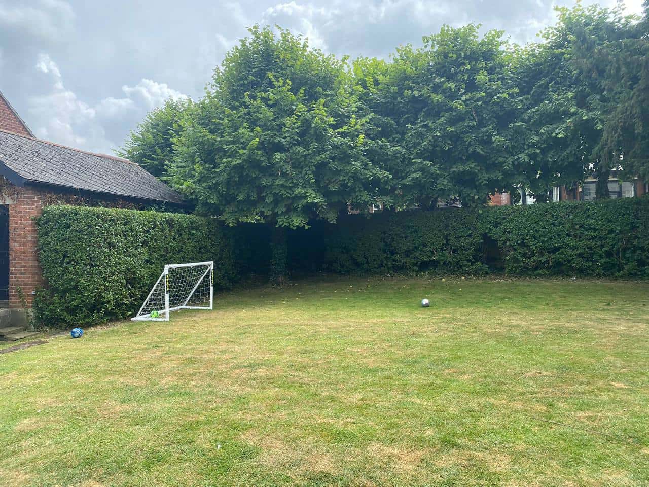 This is a photo of a hedge that has just been trimmed in a garden. The hedge is about 8 Metres long and runs along the back and left hand side of the garden iteslf. There are also trees in the background, and a house. Photo taken by Felixstowe Tree Surgeons.